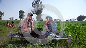 A middle-aged farmer working on a laptop while his wife is doing hand embroidery - modern villager