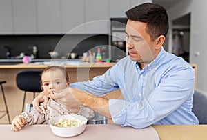 Middle-aged father feeding baby daughter at home