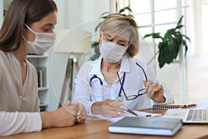 Middle aged female doctor therapist in medical mask on consultation with patient in office