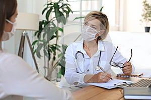 Middle aged female doctor therapist in medical mask on consultation with patient in office