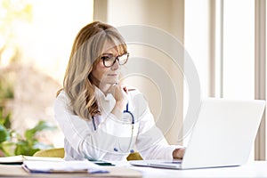 Middle aged female doctor working on laptop in doctor`s room photo