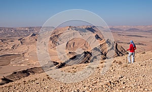 A middle aged female hiker posing on a view point with amazing panoramic view of Makhtesh Ramon desert landscape