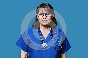 Middle aged female nurse in blue uniform with stethoscope smiling looking at camera