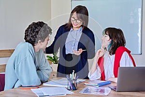 Middle aged female teacher giving lesson to teenage college students sitting at table