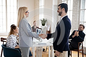 Middle aged female team leader shaking hands with young colleague.