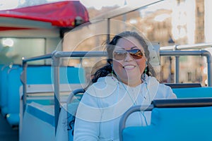 Middle-aged female tourist sitting on the open top of a tourist bus to enjoy a city tour