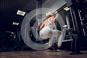 Middle-aged fitness woman doing squat exercise in a gym