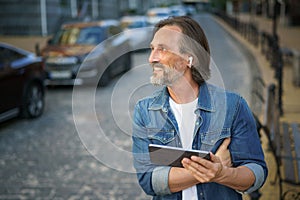 Middle aged freelancer man use gps or calling digital tablet while walking on urban streets. Mature man use wireless