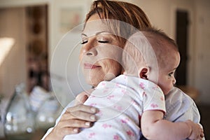 Middle aged grandmother with eyes closed holding her newborn grandson, head and shoulders, close up