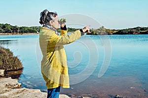 Middle-aged gray-haired brunette woman looks at birds in a lake with binoculars and points with her finger