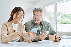 Middle aged happy couple using smartphone holding credit card buying online.