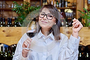 Middle aged happy woman drinking glass of red wine in restaurant