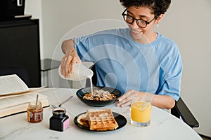 Middle-aged happy woman reading book while having breakfast at home