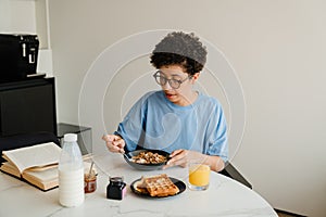 Middle-aged happy woman reading book while having breakfast at home