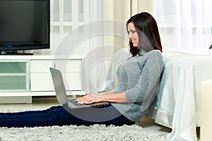 Middle-aged happy woman sitting on the floor and using laptop