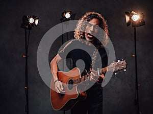 Middle aged hispanic musician in black t-shirt emotionally singing and playing guitar