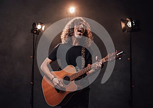 Middle aged hispanic musician in black t-shirt emotionally singing and playing guitar
