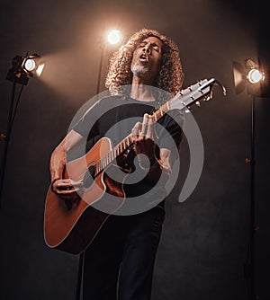 Middle aged hispanic musician in black t-shirt emotionally singing and playing guitar