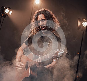 Middle aged hispanic musician emotionally playing guitar in stage lights, surrounded by smoke