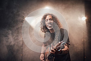 Middle aged hispanic musician emotionally playing guitar in stage lights, surrounded by smoke