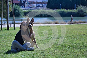 Middle-aged Hispanic woman sitting on the lawn hugging her large size tan mongrel dog with white chest. Concept love for animals,