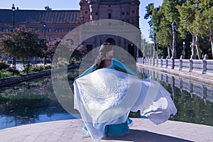 Middle-aged Hispanic woman in turquoise dress with rhinestones, belly dancing with a white veil. Belly dance concept