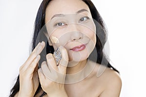 Middle-aged Japanese woman applying foundation on her cheeks