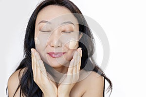 Middle-aged Japanese woman applying foundation on her cheeks