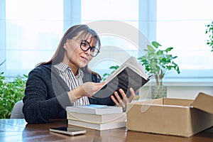 Middle-aged joyful woman with new books unpacked from cardboard box