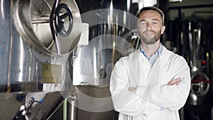 A middle-aged labouring man in a white overall standing near the factory equipment and smiling into a camera. A front