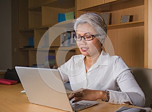 Corporate portrait of attractive and happy successful mature Asian woman working at laptop computer desk smiling confident and