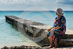 Middle aged Latin woman sitting on a stone dock alone, watching the quiet ocean