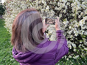 Middle Aged Latina Woman Taking a Photo of White Flowers