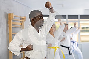 Middle-aged male attendee of karate classes practicing kata standing in row with others