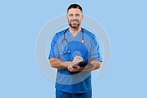 Middle aged male doctor in uniform working with patient anamnesis, standing over blue background and smiling at camera