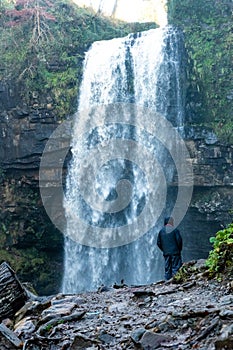 Middle aged male stood infront of Henrhyd Falls near Coelbren, the highest waterfall in South Wales, UK