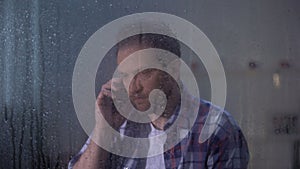 Middle-aged male talking phone with family behind rainy day, missing relatives
