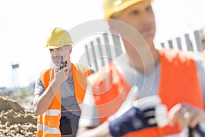 Middle-aged male worker using walkie-talkie with colleague in foreground at construction site