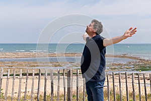 Middle aged man with arms wide open enjoying the ocean sea view