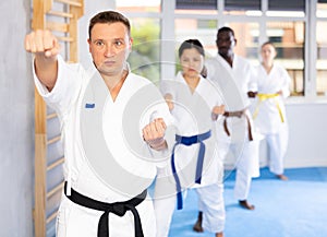 Middle-aged man attendee of karate classes practicing kata standing in row with others