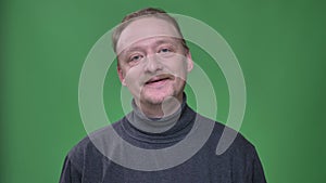 Middle-aged man with beard and moustache listening and nodding joyfully and mannerly on green background.