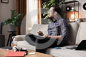 A middle-aged man with a beard is sitting on a couch with an English dictionary in his hands. The boy is trying to