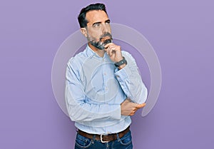 Middle aged man with beard wearing business shirt with hand on chin thinking about question, pensive expression