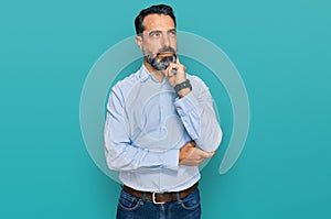 Middle aged man with beard wearing business shirt with hand on chin thinking about question, pensive expression