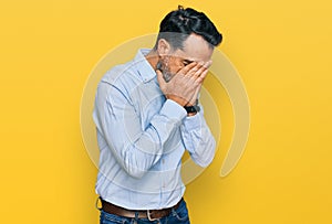 Middle aged man with beard wearing business shirt with sad expression covering face with hands while crying