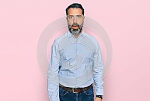 Middle aged man with beard wearing business shirt in shock face, looking skeptical and sarcastic, surprised with open mouth