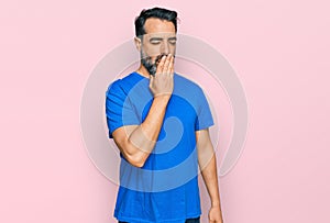 Middle aged man with beard wearing casual blue t shirt bored yawning tired covering mouth with hand