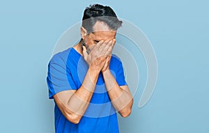 Middle aged man with beard wearing casual blue t shirt with sad expression covering face with hands while crying