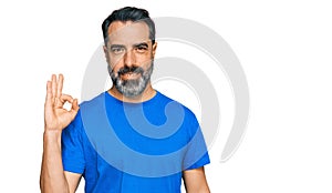 Middle aged man with beard wearing casual blue t shirt smiling positive doing ok sign with hand and fingers