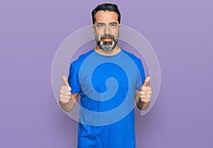 Middle aged man with beard wearing casual blue t shirt success sign doing positive gesture with hand, thumbs up smiling and happy